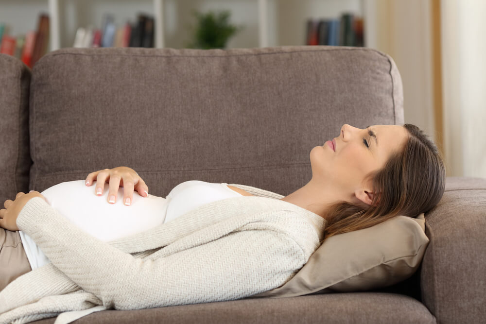 Pregnant woman suffering belly ache lying on a sofa at home