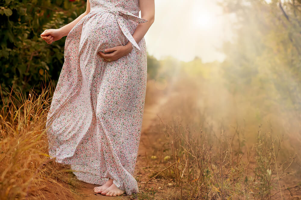 Stomach of the pregnant woman in a summer dress on the road outdoors
