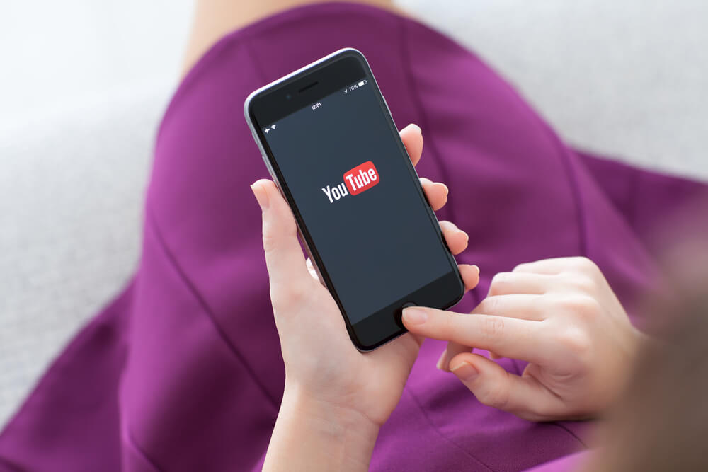 Woman holding Phone with video service YouTube on the screen.