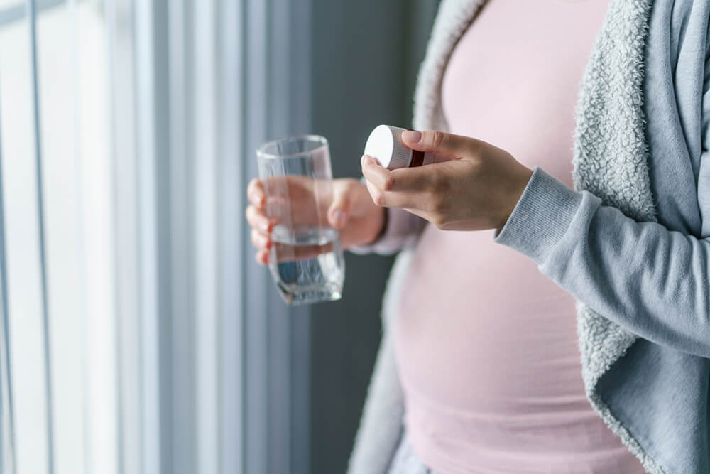 woman pregnant mother holding medicine supplement drugs and glass of water